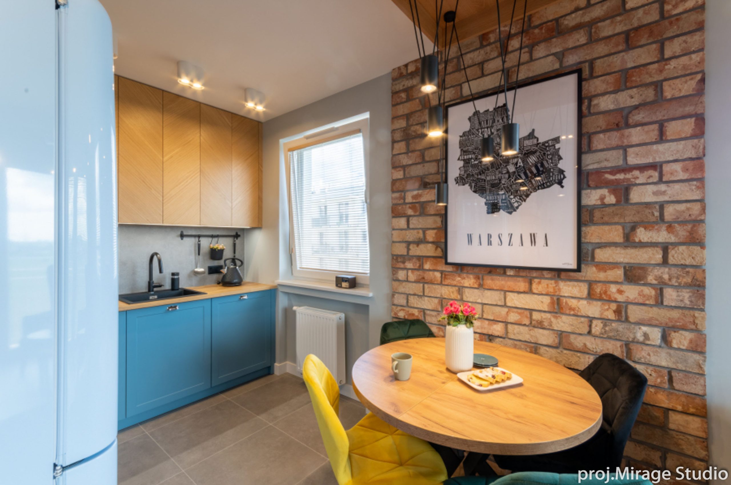 Architekt wnętrz Warszawa – loftowa kuchnia z ceglaną ścianą, drewnianymi szafkami i niebieskimi frontami.