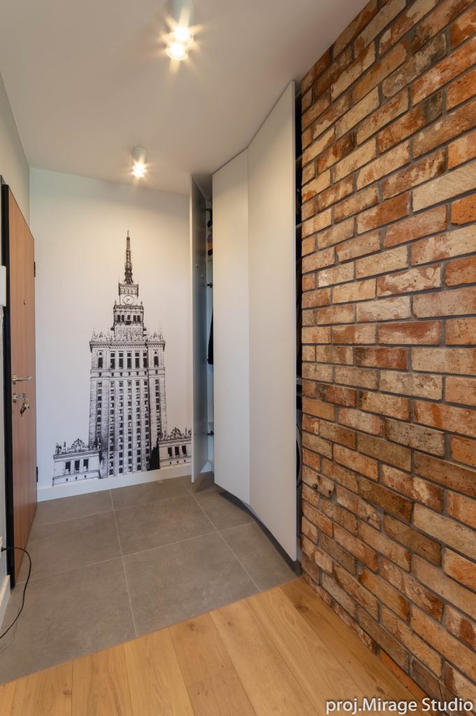 Pracownia wnętrz Warszawa. Przedpokój, mieszkanie w stylu loft, z ceglaną ścianą i fototapetą Pałacu Kultury i Nauki